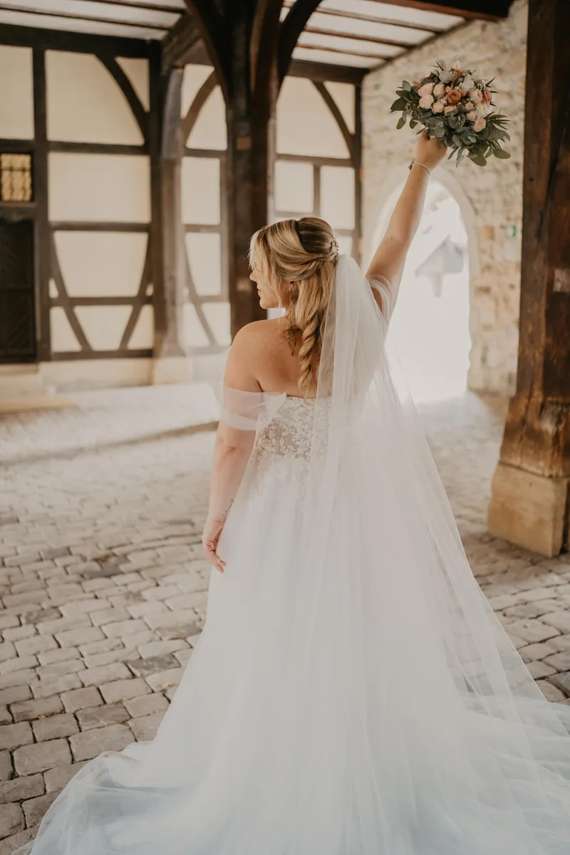 Braut mit halboffener Flechtfrisur und langem Schleier im historischen Innenhof – DK Beauty Lounge Bodelshausen