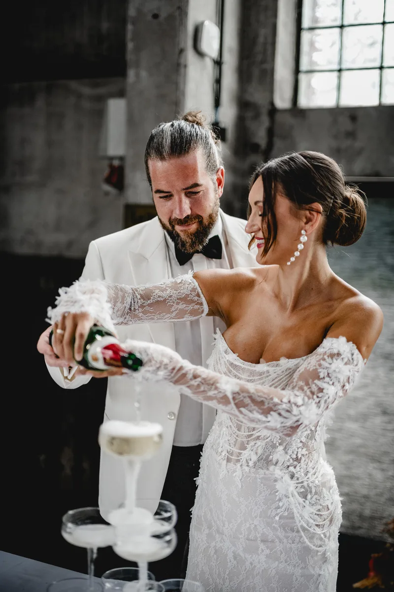 Paar beim Anstoßen, Braut mit Chignon und Perlenohrringen – Styling von Dilya Klein – DK Beauty Lounge Bodelshausen